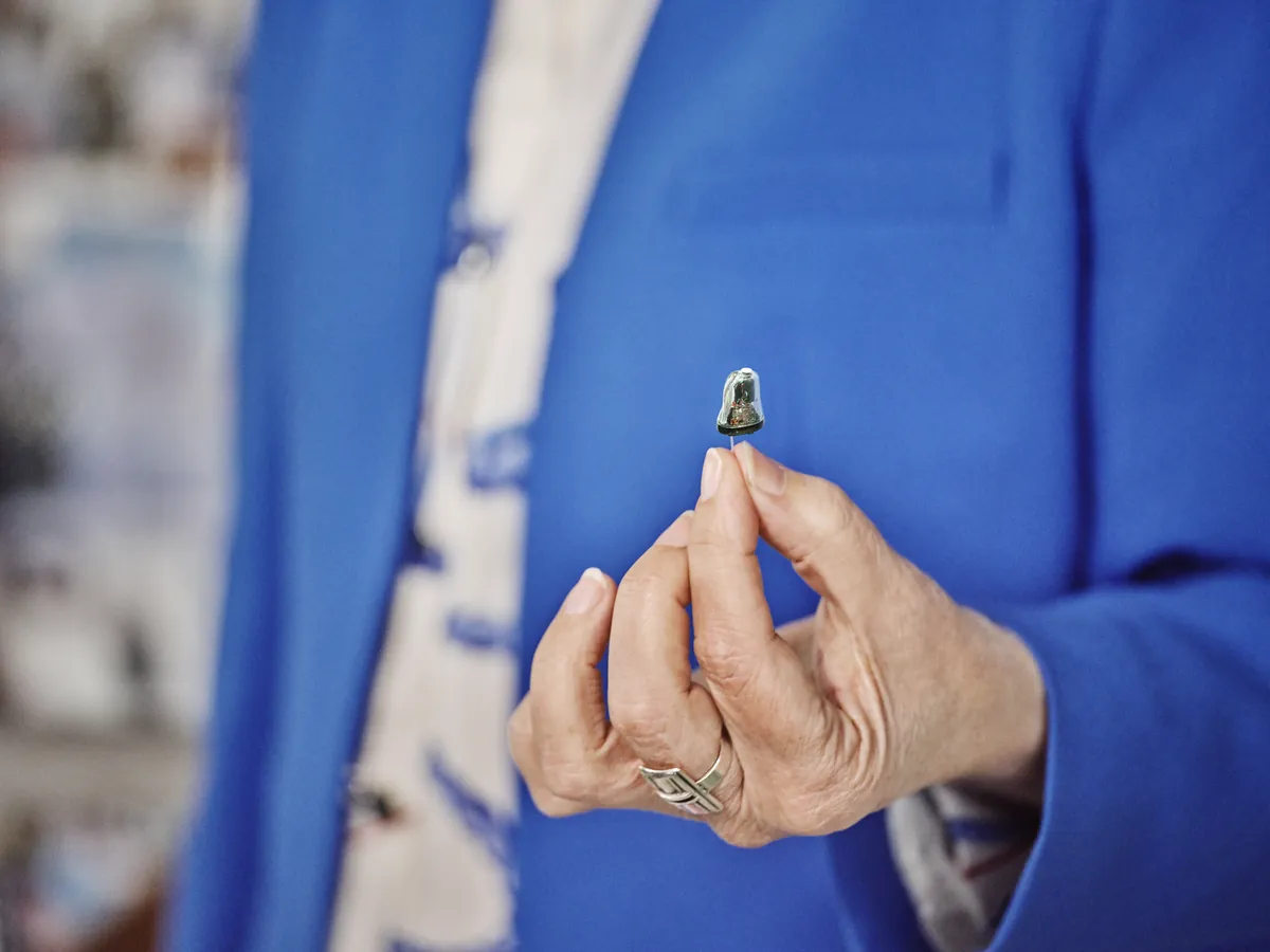 Mulher segurando um aparelho auditivo intra-auricular Oticon Own entre os dedos